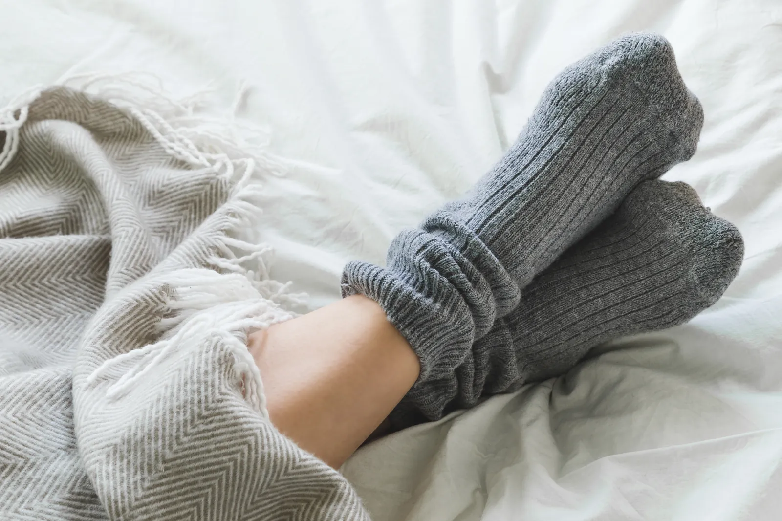 Füße in grauen Wollsocken gemütlich auf dem Bett